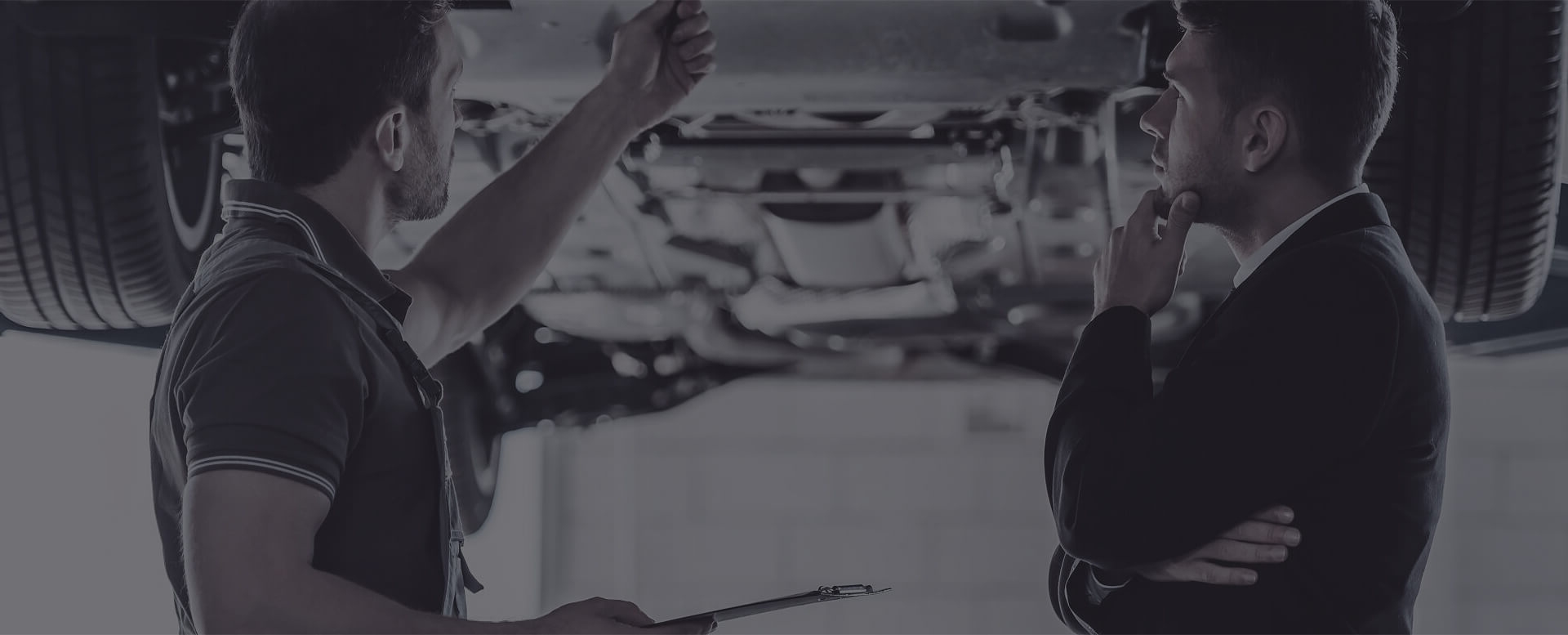 Zwei Männer stehen unter einem Auto und besprechen den Zustand des Fahrzeugs während einer Inspektion.